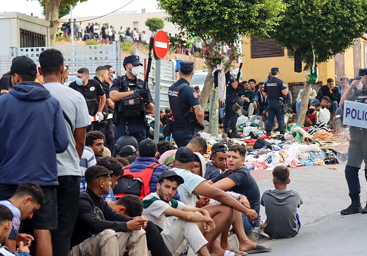 Fotografía editorial que muestra a varias personas sentadas en el suelo en la vía pública junto a agentes de policía con equipo antidisturbios en un control de seguridad.