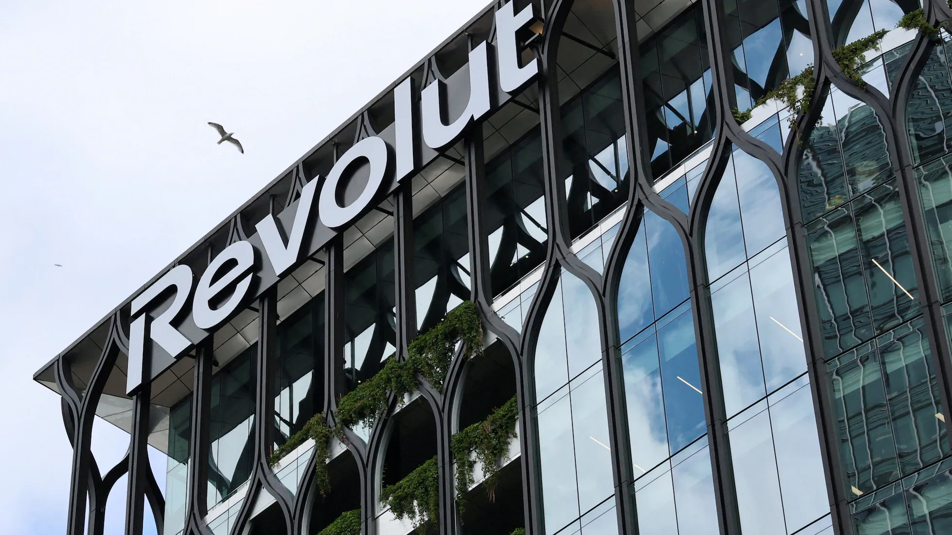 Fachada de un edificio moderno con el rótulo corporativo Revolut en la parte superior y grandes ventanales con elementos vegetales.