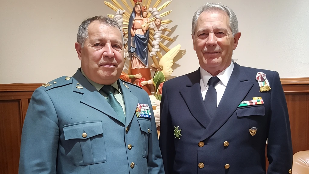 Dos hombres uniformados, uno de la Guardia Civil y otro de marinero, de pie junto a una escultura religiosa.