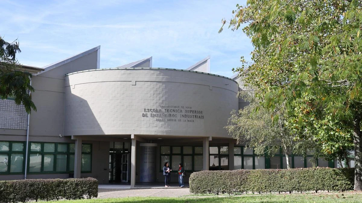 Fachada principal de la Escuela Técnica Superior de Enxeñeiros Industriais de la Universidad de Vigo, con un edificio de estructura circular central, grandes ventanales, vegetación y dos estudiantes conversando en la entrada.