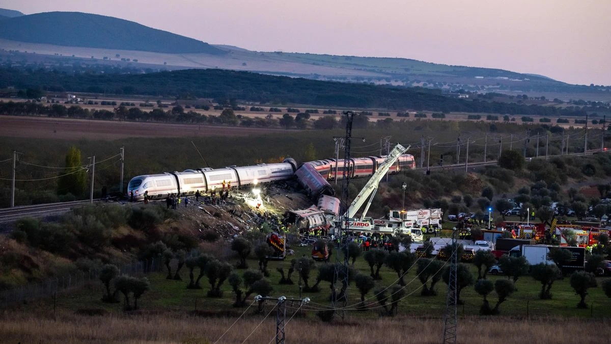 Fotografía editorial de un accidente ferroviario en España con trenes descarrilados, equipos de emergencia, grúas y personal de rescate trabajando junto a las vías.