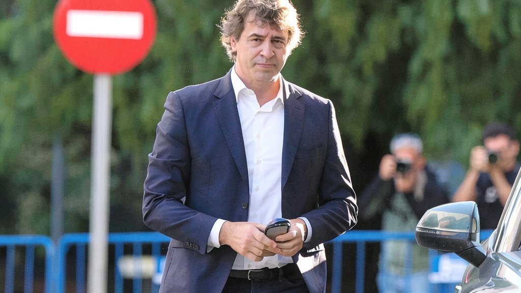 Fotografía editorial de Francisco Javier Montero Juanes, fiscal superior de Extremadura, caminando con un traje azul y camisa blanca, sosteniendo un teléfono móvil con una señal de tráfico de dirección prohibida al fondo.
