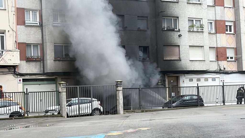 Fotografía editorial de un incendio en un garaje con densa columna de humo negro saliendo de la fachada de un edificio residencial en Santander.