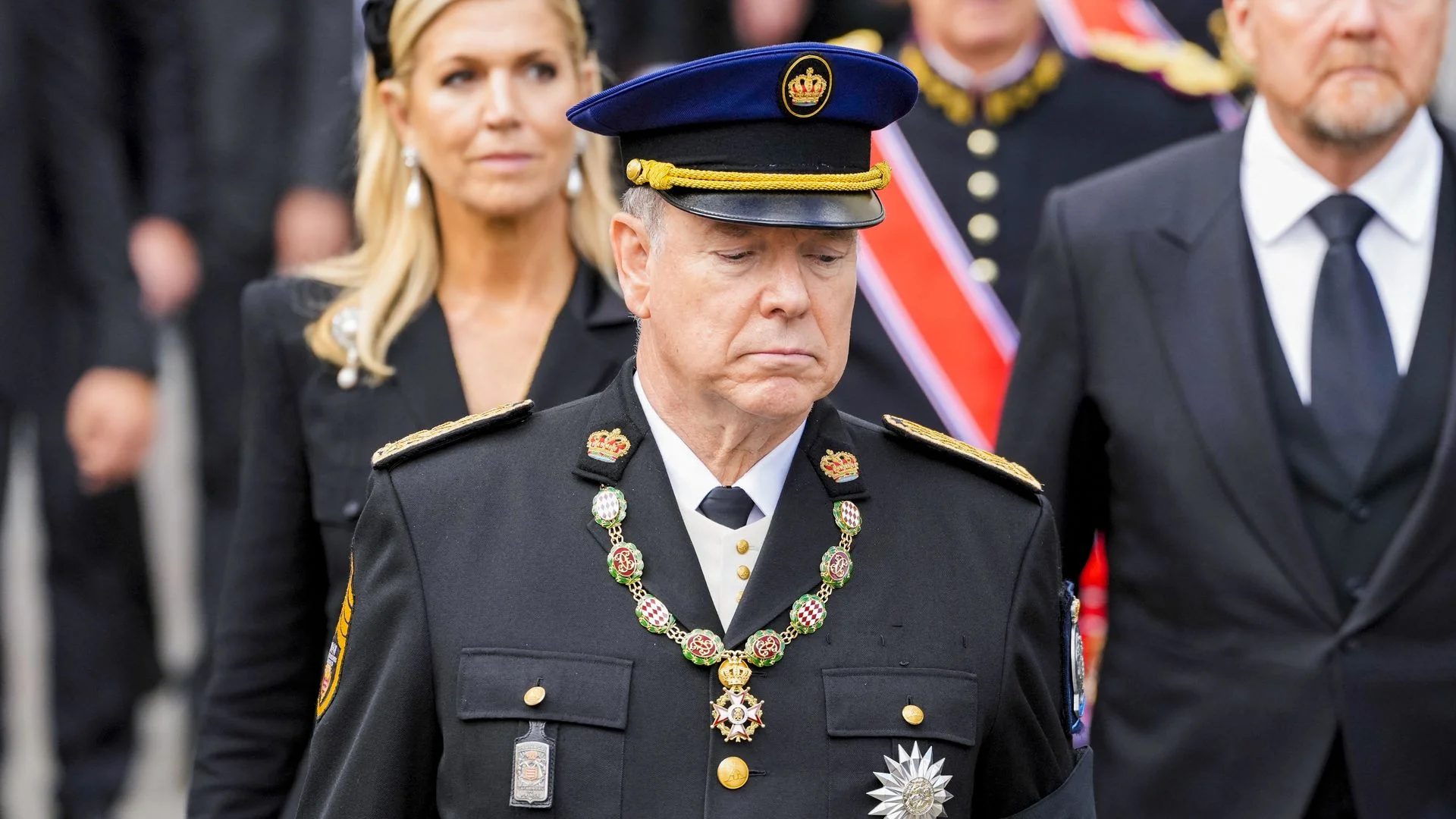 El príncipe Alberto II de Mónaco vistiendo uniforme militar de gala y condecoraciones, con la reina Máxima de los Países Bajos detrás, asistiendo a un funeral oficial.