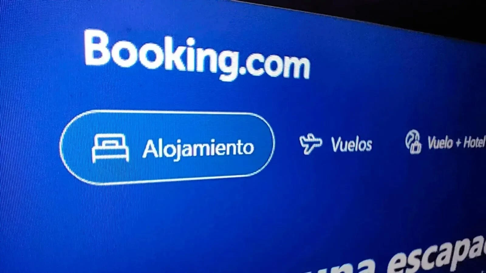 Pantalla de televisión mostrando el logotipo y la interfaz de Booking.com en español con las opciones de Alojamiento, Vuelos y Vuelo + Hotel.