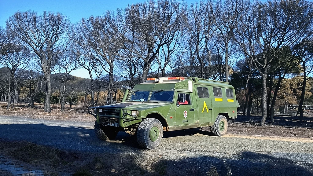 Vehículo militar todoterreno táctico Uro Vamtac estacionado en una zona boscosa con árboles quemados.