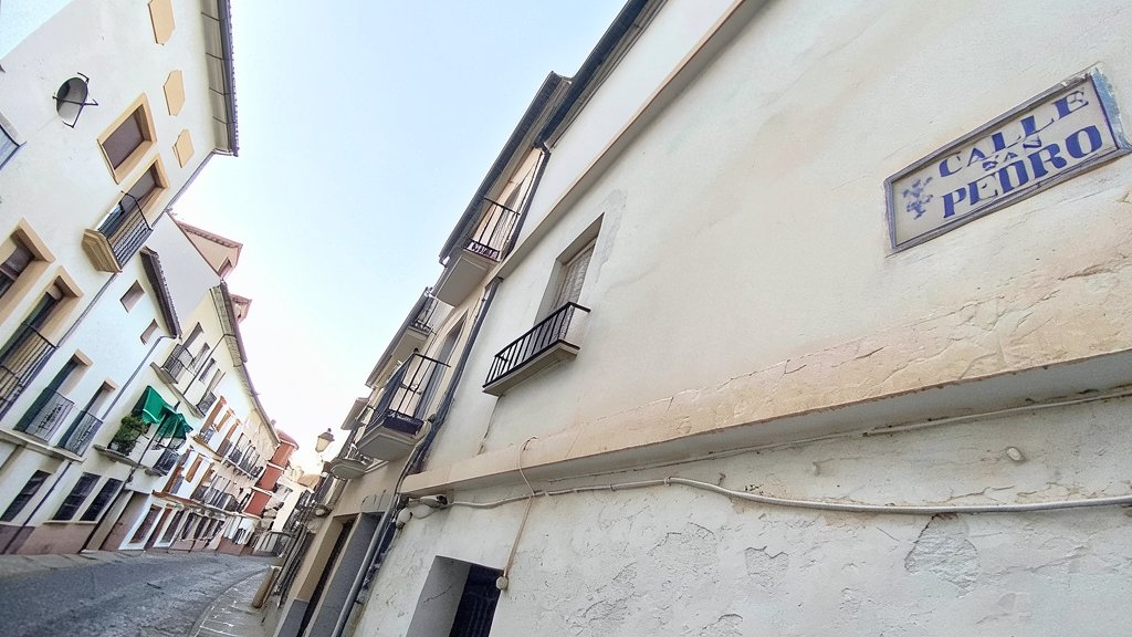 Fotografía contrapicada de una calle estrecha y empinada con edificios blancos tradicionales y el rótulo de la calle San Pedro en la fachada