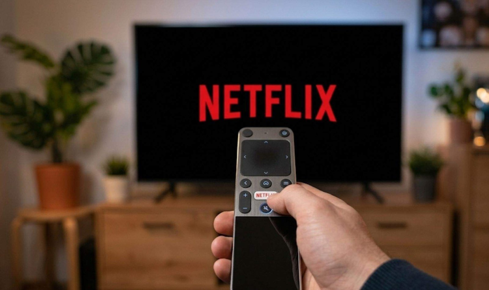 Persona sosteniendo un mando a distancia frente a un televisor que muestra el logotipo de Netflix.