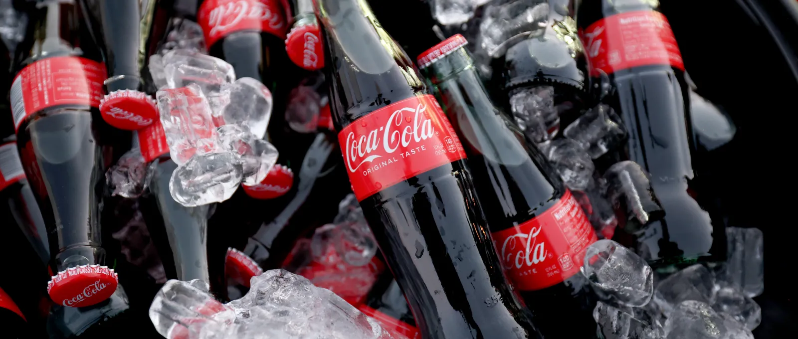 Primer plano de botellas de cristal de Coca-Cola frías sobre hielo picado en una cubitera.