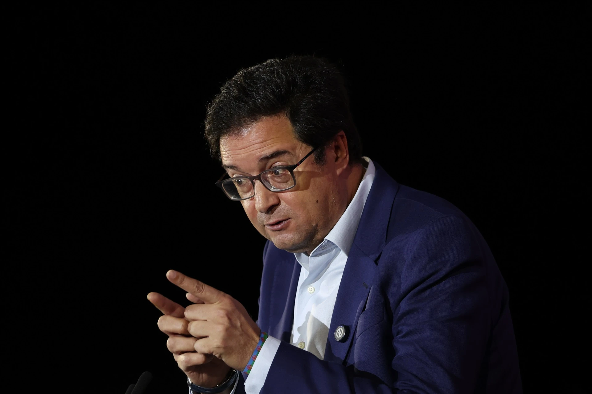 Fotografía de medio plano de Óscar López con traje azul y camisa blanca, gesticulando con las manos durante una intervención política.