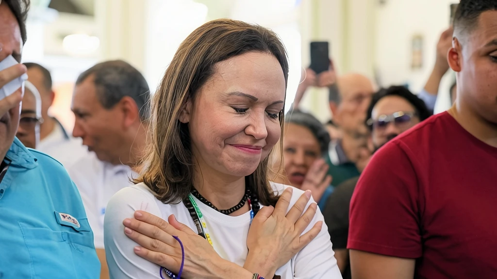 María Corina Machado con expresión emotiva cruzando los brazos sobre el pecho en un santuario religioso rodeada de simpatizantes