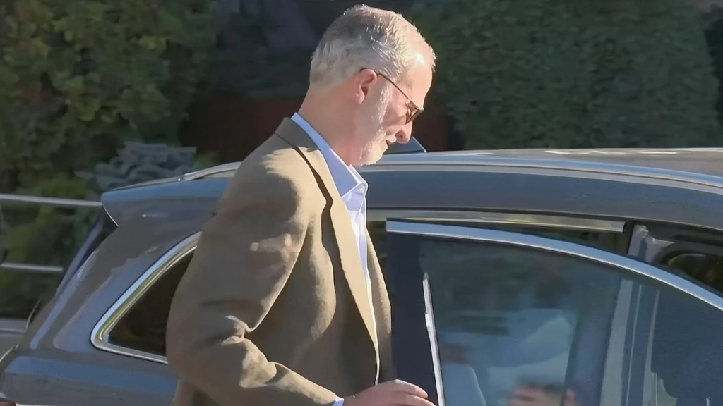 Hombre con chaqueta marrón y camisa clara saliendo de un coche oscuro.