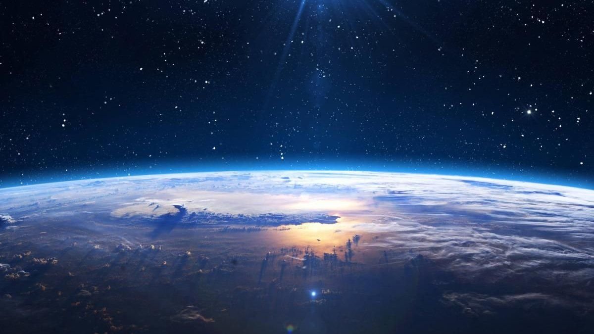 Vista panorámica de la Tierra desde el espacio exterior, mostrando la curvatura del planeta con la atmósfera iluminada y un cielo estrellado.