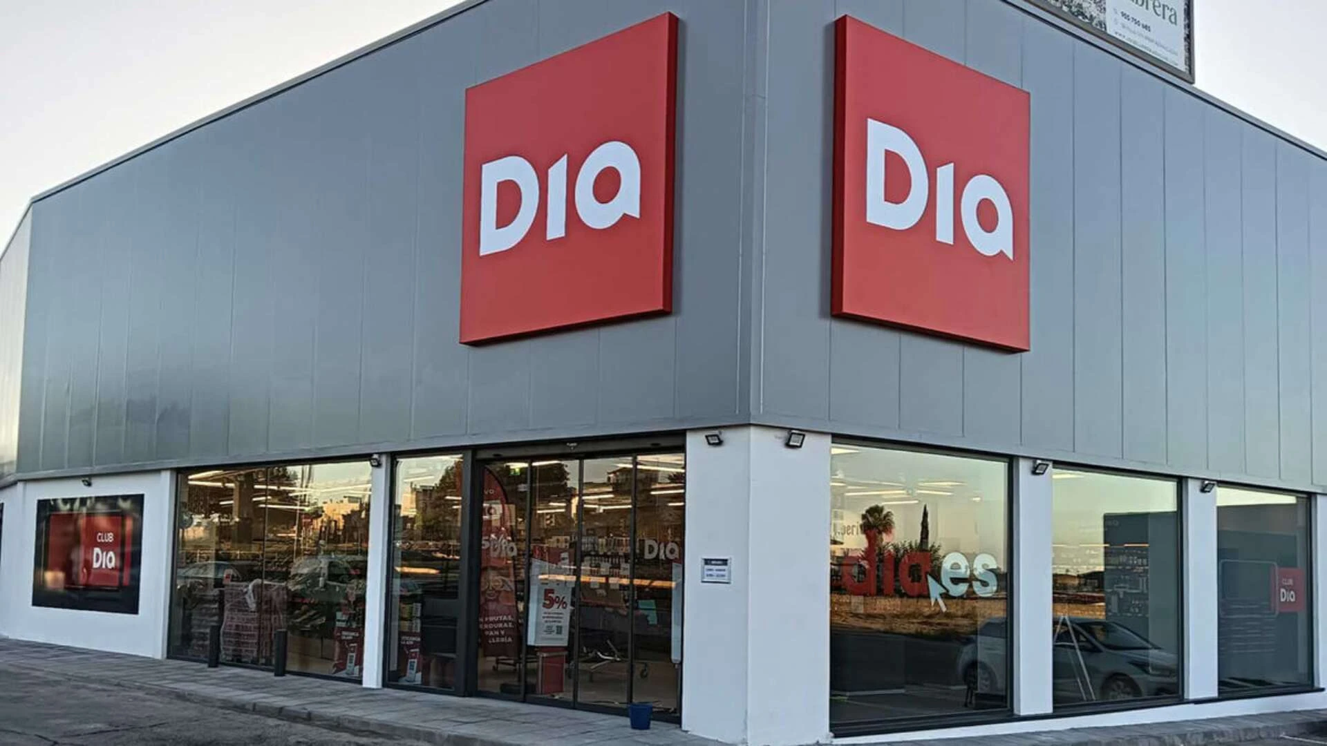 Fachada exterior de un supermercado DIA con grandes rótulos rojos y escaparates acristalados en una zona urbana.