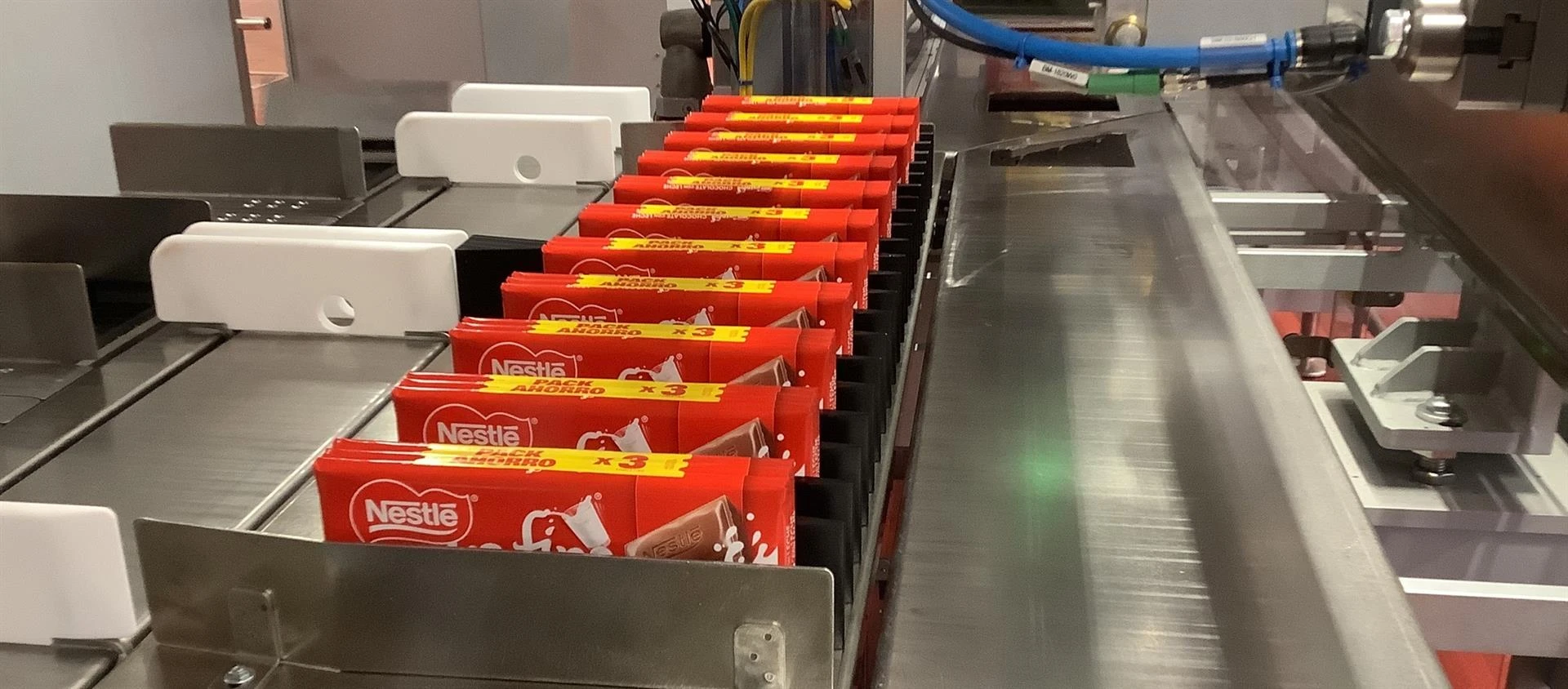 Línea de producción automatizada con tabletas de chocolate Nestlé avanzando sobre una cinta transportadora metálica en una fábrica.